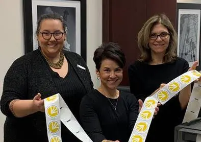 Three women holding rolls of printed yellow labels
