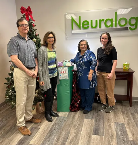 Neuralog team members beside a Christmas tree and the toy drive donation box